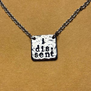 May include: A silver necklace with a square pendant that says "I dissent".
