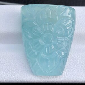 May include: A carved aquamarine gemstone with a floral design. The gemstone is a light blue color and has a smooth, polished finish.