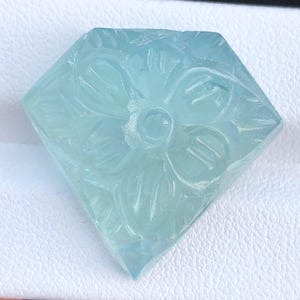 May include: A carved aquamarine gemstone in the shape of a diamond with a flower design.