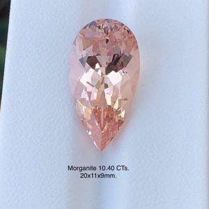 May include: A pear-shaped morganite gemstone with a peach hue. The gem is faceted, displaying internal reflections. The image includes text indicating the gemstone weighs 10.40 carats and measures approximately 0.79 x 0.43 x 0.35 inches.