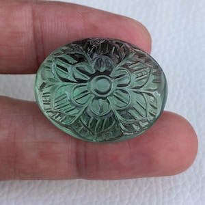 May include: A green carved gemstone cabochon with a floral design. The cabochon is round and has a smooth, polished surface.
