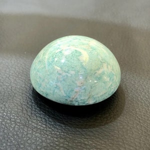 May include: A smooth, rounded stone with a mottled pattern of light blue and white. The stone has a polished surface and a natural, organic shape. The stone is a light blue color with white veining.