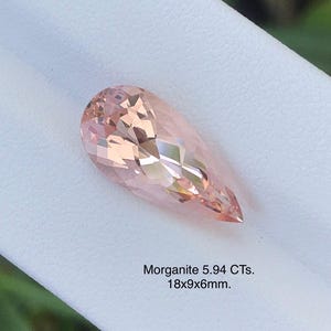 May include: A pear-shaped morganite gemstone with a faceted cut, displaying a soft peach color. The gemstone is 18mm long, 9mm wide, and 6mm thick. The text on the image reads "Morganite 5.94 CTs. 18x9x6mm."