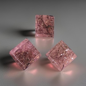 May include: Three pink carved glass squares with a floral design. The glass is translucent and has a slight sparkle.