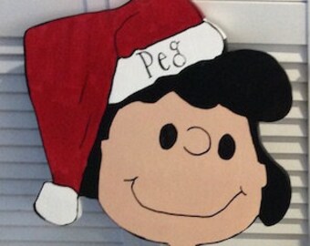 May include: A wooden cutout of a cartoon girl wearing a green dress and a red Santa hat with the name "Peg" written on it.