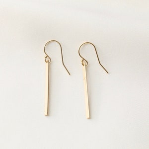 May include: A pair of gold dangle earrings with thin, straight bars hanging from the hooks.