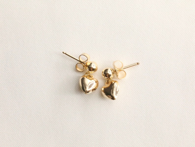 May include: A pair of gold heart-shaped earrings with a small ball at the top of each heart.