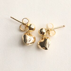 May include: A pair of gold heart-shaped dangle earrings with a small ball at the top of each earring.