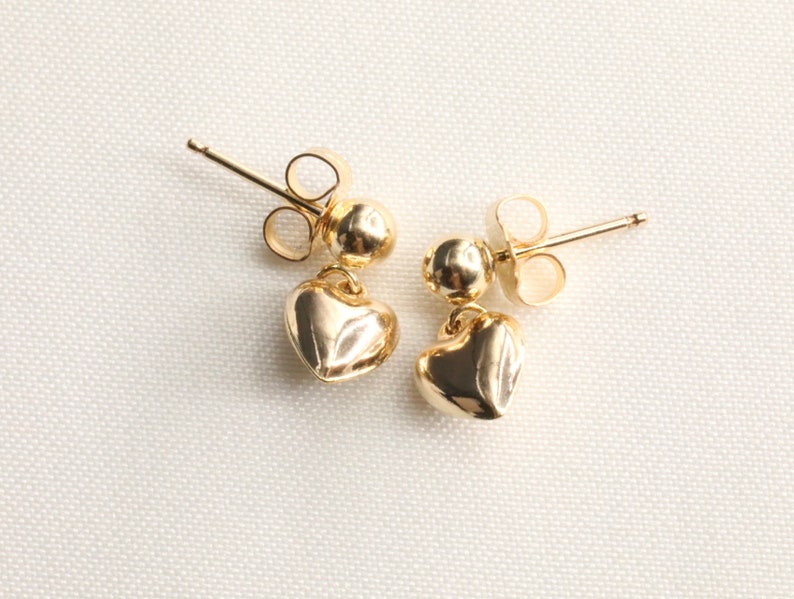 May include: A pair of gold heart-shaped dangle earrings with a small ball at the top of each earring.