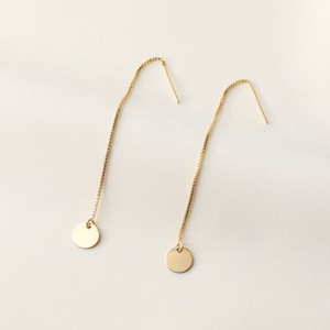 May include: A pair of gold dangle earrings with small round discs at the end of each chain.