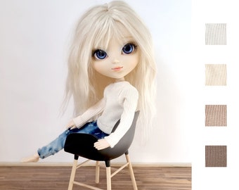 May include: A doll with long blonde hair wearing a white sweater and blue jeans sits on a black and wooden chair. The doll has blue eyes and is looking at the camera.
