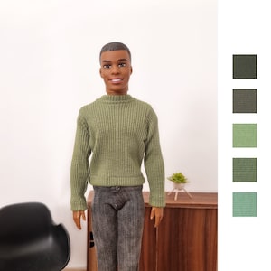 May include: A doll wearing a green ribbed sweater and gray pants. The doll has short black hair and brown eyes.