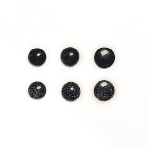 May include: Six black round cabochon stones with a glittery finish. The stones are arranged in two rows of three.