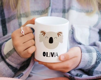 Könnte beinhalten: Weiße Keramiktasse mit einem Cartoon-Koala-Gesicht und dem Namen "Olivia" auf dem Boden.
