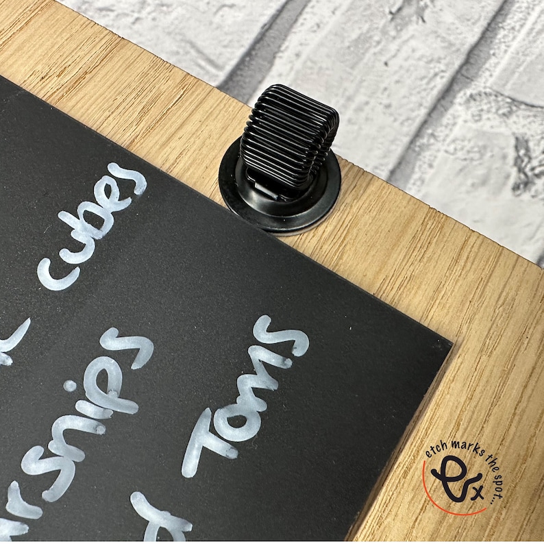 May include: A black chalkboard with white chalk writing that says "cubes", "snips", and "Toms". A black metal clip is attached to the top of the chalkboard.