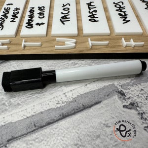 May include: A white dry-erase marker with a black cap and a sponge eraser. The marker is lying on a white surface with a black and white pattern.