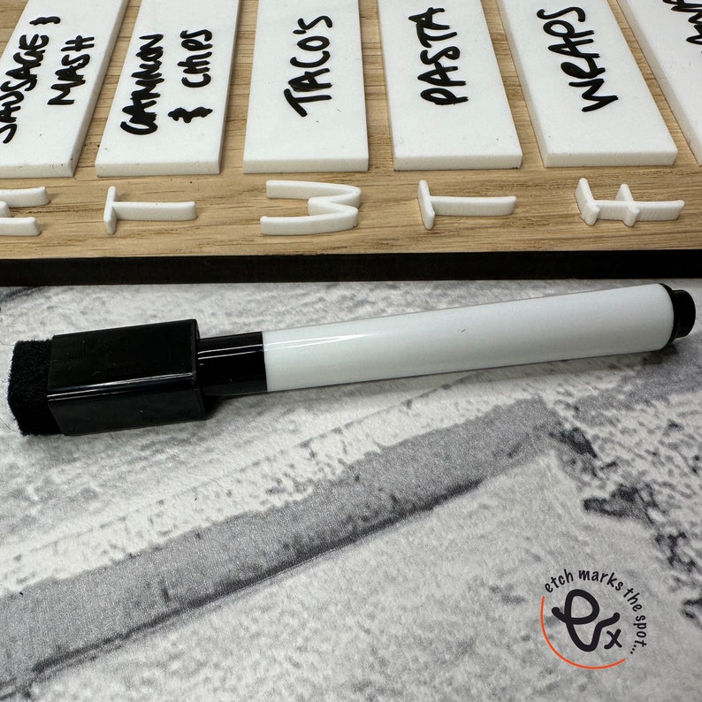 May include: A white dry-erase marker with a black cap and a sponge eraser. The marker is lying on a white surface with a black and white pattern.