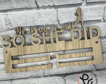 May include: Wooden medal display with the text "She believed she could so she did" and a silhouette of a woman running. The display has two rows for hanging medals.