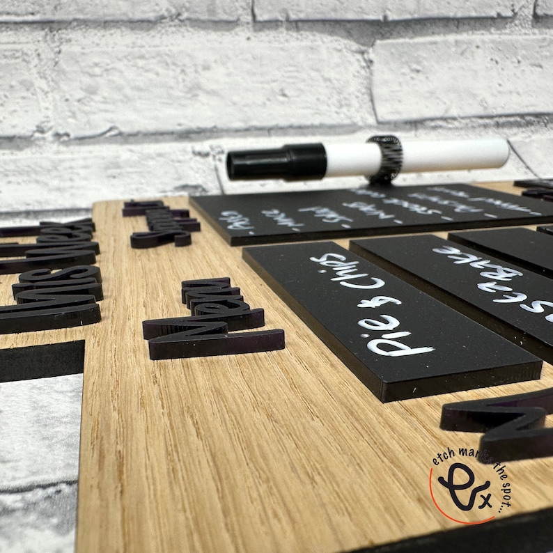 May include: A wooden sign with black chalkboard inserts for writing. The sign has the words "Mrs. Smith's" and "Menu" written on it. The chalkboard inserts have the words "Pie & Chips", "Sausage", and "Fish & Chips" written on them. A white dry erase marker is lying on top of the sign.