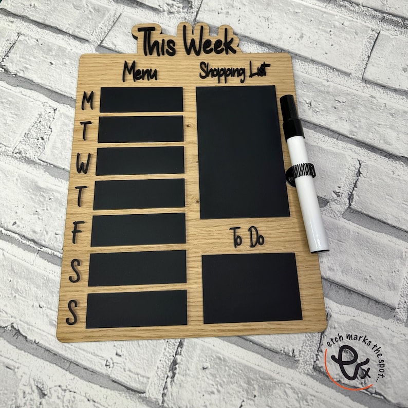 May include: A wooden weekly planner with a chalkboard surface. The planner has sections for "This Week", "Menu", "Shopping List", and "To Do". It comes with a white dry-erase marker.