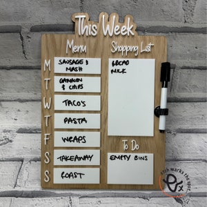 May include: A wooden weekly meal planner with a white dry-erase surface. The planner has a section for "This Week", "Menu", and "Shopping List". The "Menu" section has a list of days of the week with a space for writing in meals. The "Shopping List" section has a space for writing in a shopping list. The "To Do" section has a space for writing in a to-do list. The planner has a black dry-erase marker attached to it.