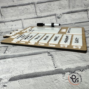 May include: A white dry-erase meal planner with a wooden frame. The planner has sections for each day of the week and includes categories for different types of meals, such as "Sausage, Mash & Veg", "Tacos", "Pasta", "Wraps", "Takeaway", "Roast", and "Eat In".