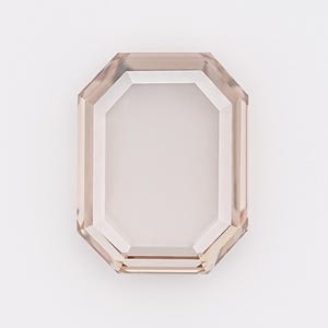 May include: A faceted, rectangular gemstone with a light brown hue. The gem has an emerald cut with a clear, rectangular center and a beveled edge. The gemstone is set against a white background.