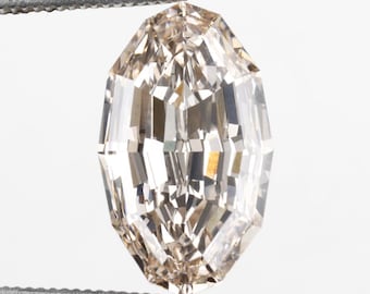 May include: A light brown, oval-cut diamond held by tweezers against a white backdrop. The diamond's facets reflect light, creating a sparkling effect. The tweezers are silver-coloured.