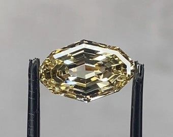May include: A loose, marquise-shaped gemstone with a light yellow hue and a faceted surface. The stone features a symmetrical, elongated design with sharp points at both ends and is held by a pair of black-tipped metal tweezers.