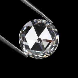 May include: A clear, round-cut diamond held by silver tweezers against a black background. The diamond's facets reflect light, creating a brilliant sparkle. The gem is a focal point, showcasing its clarity and cut.