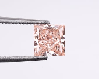 May include: A square-shaped, light pink diamond gemstone with a faceted cut. The diamond is held by tweezers against a white background.