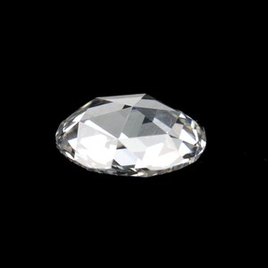 May include: A clear, faceted gemstone with a brilliant cut, resting against a black background. The gem's multiple facets reflect light, creating a sparkling effect. The overall shape is oval.