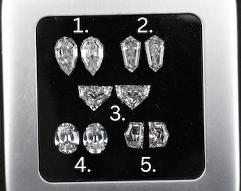 May include: An assortment of five pairs of cut diamonds, each with a unique shape. The diamonds are displayed on a dark surface, showcasing their facets and brilliance. Shapes include pear, kite, half-moon, oval, and a geometric design.