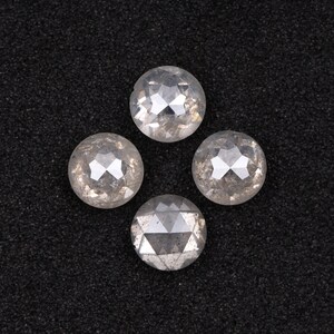 Puede incluir: Cuatro piedras preciosas redondas, facetadas, transparentes y blancas sobre un fondo negro.