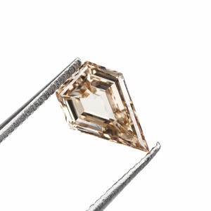 May include: A kite-shaped, light brown diamond held by silver tweezers. The gemstone has multiple facets, reflecting light. The diamond is set against a white background, highlighting its clarity and shape. The overall image is a close-up shot.