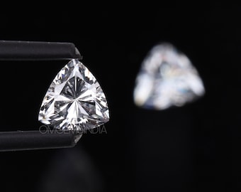 May include: A clear, triangular gemstone with a star-shaped pattern inside. The gemstone is held by a pair of tweezers against a black background.