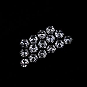 Puede incluir: Una colecci&oacute;n de catorce piedras preciosas sueltas, transparentes, incoloras y de corte hexagonal dispuestas en un grupo. Cada piedra presenta una superficie facetada que refleja la luz, creando un aspecto brillante y centelleante sobre un fondo negro.