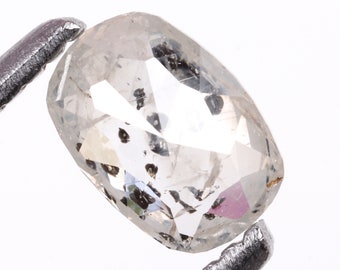 May include: A clear, oval-shaped diamond with black inclusions. The diamond is set in a silver setting.