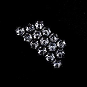 Puede incluir: Una colecci&oacute;n de catorce piedras preciosas transparentes e incoloras, con corte hexagonal y dispuestas en grupo. Cada piedra presenta una superficie facetada que refleja la luz, creando un aspecto brillante y centelleante sobre el fondo negro.
