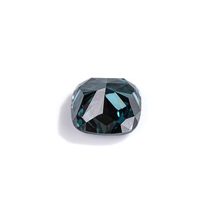 May include: A faceted, cushion-cut gemstone with a deep teal color. The gem is set against a white background, showcasing its multiple reflective surfaces. The overall shape is a rounded rectangle, with a high degree of clarity.