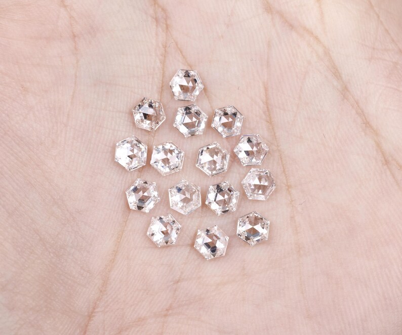 Puede incluir: Una colecci&oacute;n de catorce peque&ntilde;as piedras preciosas transparentes de corte hexagonal con superficies facetadas. Cada piedra presenta una forma geom&eacute;trica de seis lados y una apariencia reflectante y transparente.