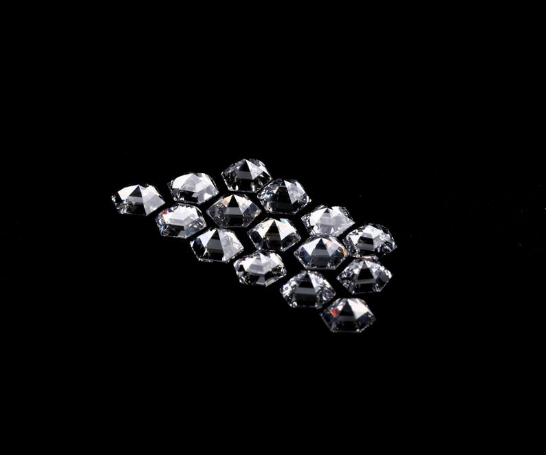 Puede incluir: Una colecci&oacute;n de peque&ntilde;as piedras preciosas transparentes y facetadas dispuestas en un grupo. Cada piedra presenta una forma hexagonal con m&uacute;ltiples facetas triangulares que reflejan la luz, creando un aspecto brillante y centelleante.