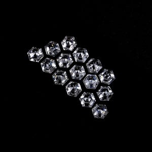 Puede incluir: Una colecci&oacute;n de catorce piedras preciosas transparentes e incoloras, con corte hexagonal y dispuestas en grupo. Cada piedra presenta una superficie facetada que refleja la luz, creando un aspecto brillante y centelleante sobre el fondo negro.