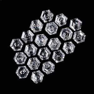 Puede incluir: Una colecci&oacute;n de diecinueve piedras preciosas transparentes e incoloras, con corte hexagonal y dispuestas en grupo. Cada piedra presenta una superficie facetada con un patr&oacute;n geom&eacute;trico que refleja la luz, creando un aspecto brillante y centelleante sobre un fondo negro.