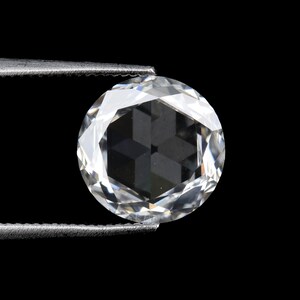 May include: A round, faceted diamond held by tweezers against a black background. The diamond is clear and reflects light, showcasing its many facets and internal structure. The tweezers are silver.