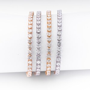K&ouml;nnte beinhalten: Vier zarte Armb&auml;nder, jedes mit einer Reihe funkelnder, klarer Edelsteine. Die Armb&auml;nder sind in Ros&eacute;gold-, Silber- und Goldt&ouml;nen gehalten und schaffen eine luxuri&ouml;se und elegante &Auml;sthetik. Die Edelsteine sind eng aneinander gesetzt.