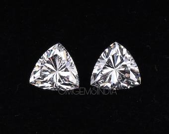 May include: Two brilliant-cut, triangular gemstones with a multitude of facets, reflecting light. The gems are set against a black background, showcasing their clarity and sparkle. The gems are likely for jewelry.
