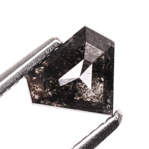 May include: A black diamond with a square shape and a faceted cut. The diamond is held in tweezers.