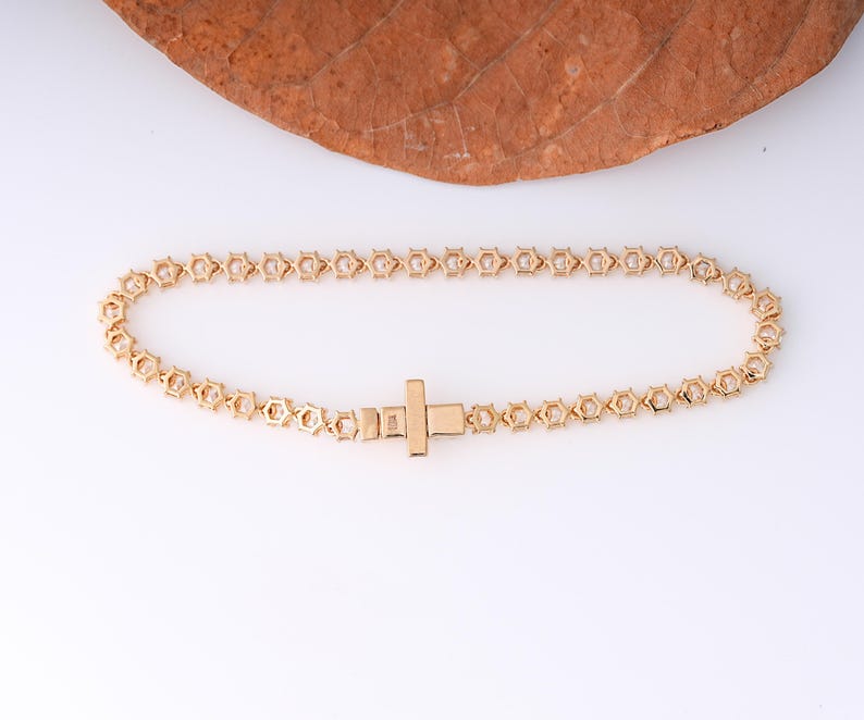 K&ouml;nnte beinhalten: Ein goldfarbenes Armband mit geometrischem Design. Das Armband hat eine Reihe von sechseckigen Formen, die miteinander verbunden sind, mit einem rechteckigen Verschluss. Das Armband wird auf einer wei&szlig;en Oberfl&auml;che pr&auml;sentiert.