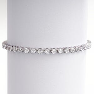 K&ouml;nnte beinhalten: Ein silbernes Armband mit einer Reihe von sechseckigen, klaren Edelsteinen. Das Armband wird vor einem wei&szlig;en Hintergrund pr&auml;sentiert, der sein filigranes Design und seinen Glanz hervorhebt. Die Edelsteine sind gleichm&auml;&szlig;ig angeordnet.